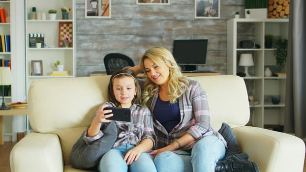 Little girl laughing while watching a video on smartphone sitting on the couch with her mother.