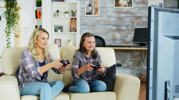 Beautiful young mother playing video games with her daughter using wireless controller.