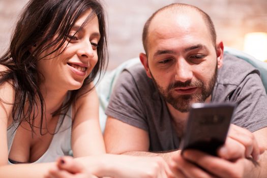 Close up of young couple wearing pajamas using smartphone.