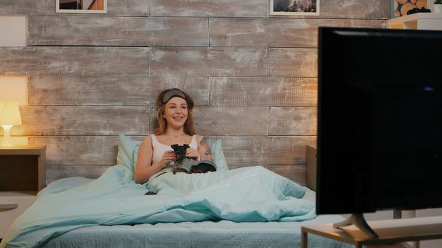 Zoom in shot of beautiful woman in pajamas at night watching tv with her dog.