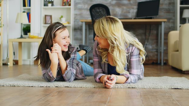 Little girl with braces lying on the floor with her mother. Cheerful family.