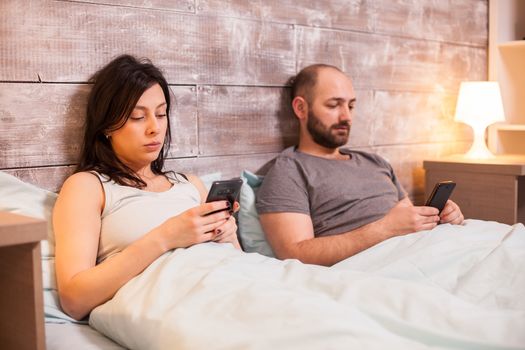 Bored caucasian couple before going to sleep browsing on smartphone.