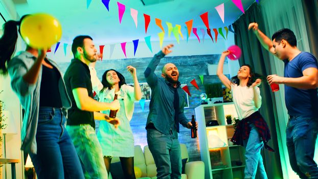 Cheerful group of young people dancing and socializing at the party. Apartment with neon lights.