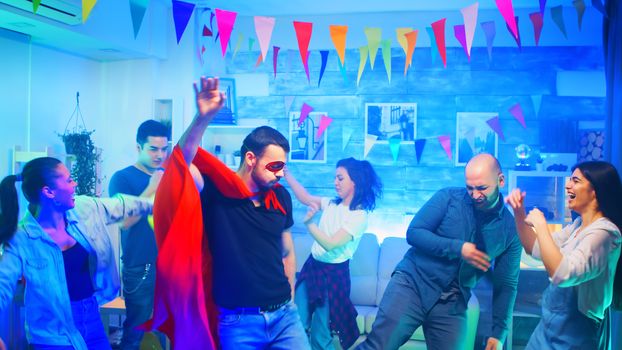 Cheerful young man wearing a superhero red cape showing his dancing moves at his friends party.