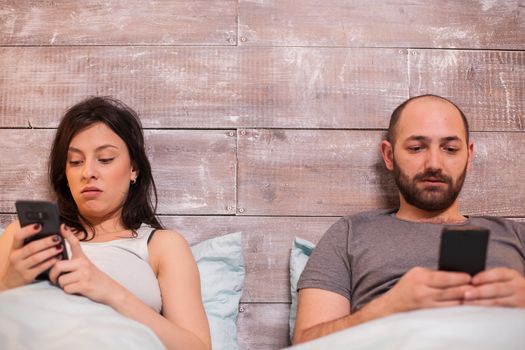 Young couple in bed late at night using smartphone. Comfortable bed.