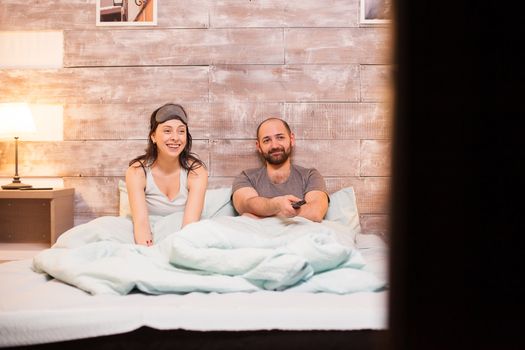 Cheerful couple in pajamas watching a comedy movie on big tv.