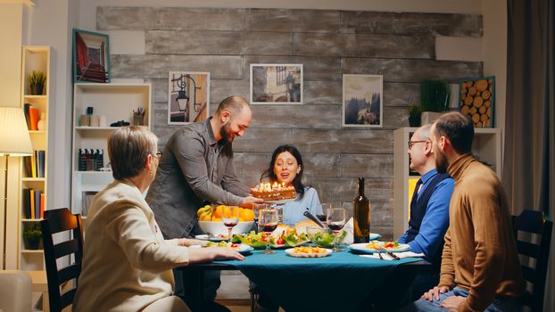 Beautiful young woman blowing candles on birthday cake. Delicious cake. Family dinner. Slow motion shot