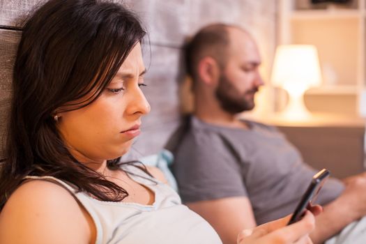 Confused young woman while using her phone before going to sleep on cozy bed.