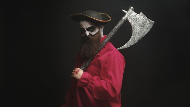 Scary bearded man holding an axe dressed up like a pirate for halloween.