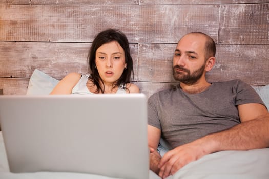 Beautiful couple spending time in on laptop before bedtime. Couple in pajamas