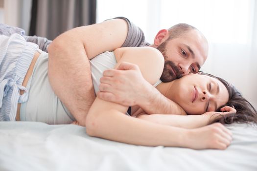 Portrait of bearded man snuggle with his girlfriend in the morning while she's sleeping.