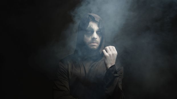 Man dressed up like grim reaper for halloween party over a black background with smoke