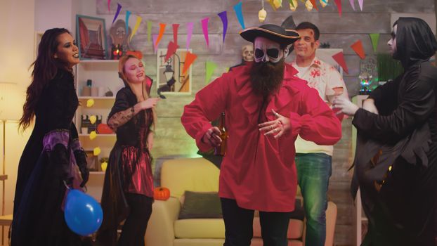 Bearded man dressed up like a pirate celebrating halloween with his friends in a thematic decorated party room