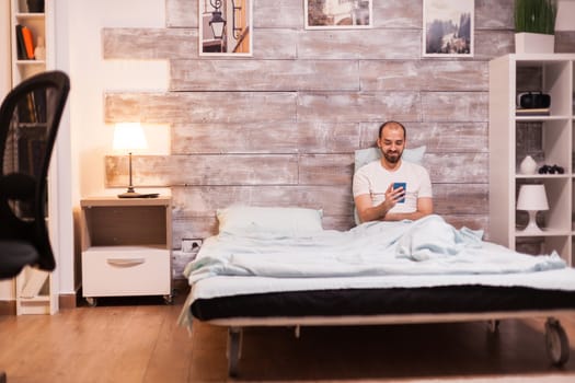 Young man smiling using smartphone before going to sleep.