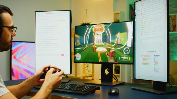 Zoom in shot of young man playing shooter games using wireless controller on powerful PC with two streaming chats opened