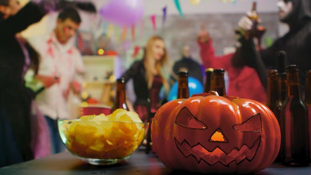 Scary pumpkin on the party while group of people are dancing celebrating halloween in the background