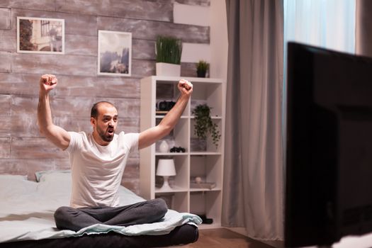 Excited sports fan in bed at night watching a football match.