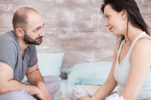 Husband and wife wearing pajamas looking at each other after waking up in the morning.