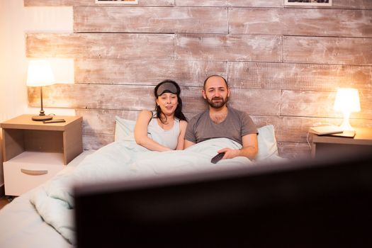 Young couple in pajamas relaxing watching tv after a hard day at work.