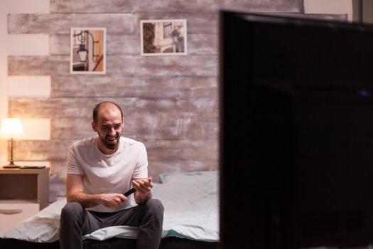 Amused man in front of tv at night during a reality show.