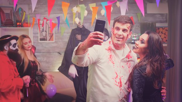 Dangerous zombie and spooky witch taking a selfie at halloween party in decorated house