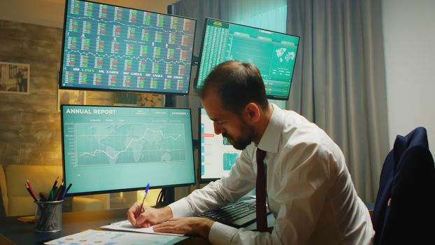 Stock market trader pointing at monitor computer and taking notes. Financial crash.