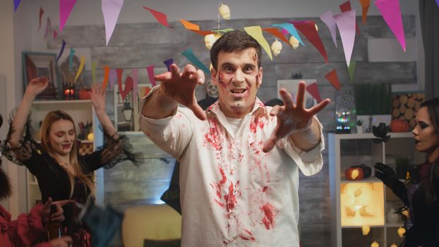 Young man with zombie disguise celebrating halloween with his friends at a wild disco house party.