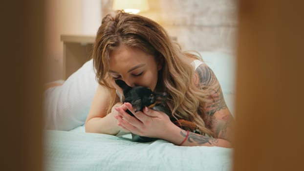 Happy young woman in pajamas playing with her dog in bed.