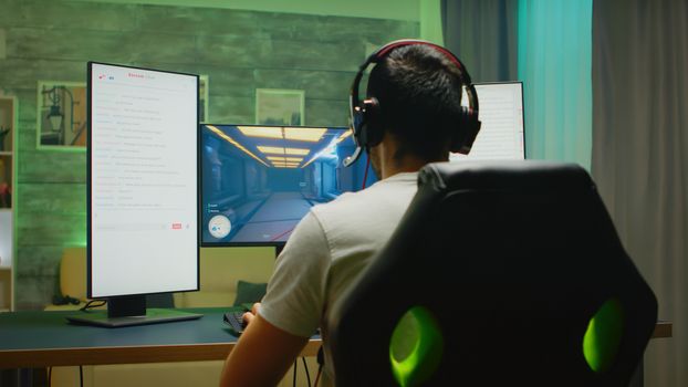 Back view of professional gamer streaming his competition on triple monitor setup with two streaming chats open