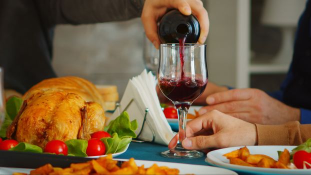 Close up of young man pouring red wine to his father at family gathering.