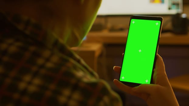 Back view of young woman holding smartphone with green screen.