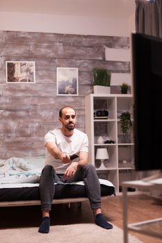 Cheerful man watching tv show at night wearing pajamas.