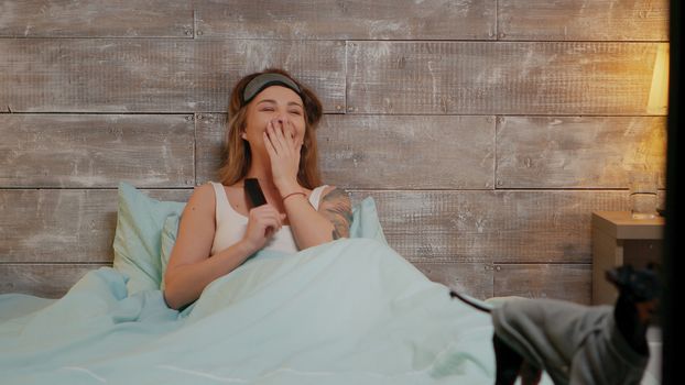 Attractive young woman in pajamas laughing while watching tv at night. Happy dog.