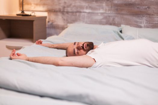 Tired man falling asleep on his back on comfortable bed.