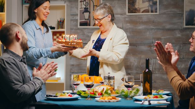 Senior woman celebrating her birthday with the family. Delicious cake at gathering with friends and family. Slow motion shot