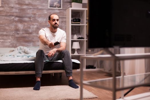 Guy in pajamas at night in bed watching a movie on big tv.