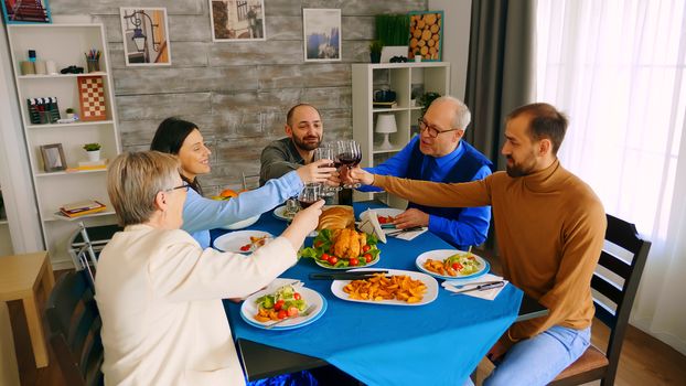 Top view of family clinking glasses with red wine while making a toast during dinner with delicious food.