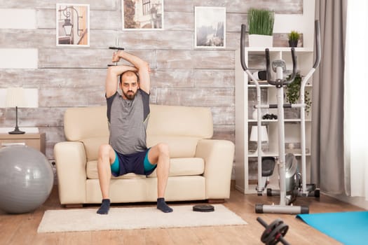 Man in shape doing triceps exercise with dumbbell during global pandemic.