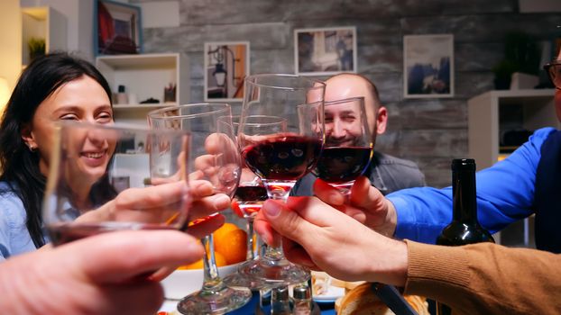 Zoom in shot of family clinking glasses of red wine at dinner over the table.