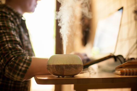 Woman working on laptop from home during covid-19 with essential oil diffuser on table.