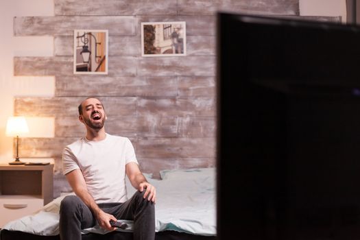 Shot of cheerful man at night in bedroom watching tv.