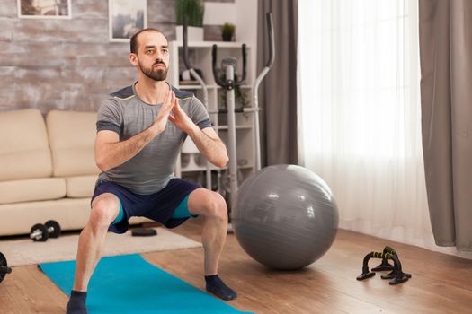 Athletic man doing squats for legs during self isolation.