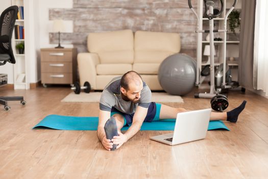 Athletic man stretching on yoga mat following online training during global pandemic.