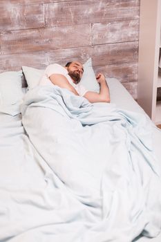 Tired man resting under the blanket in his comfortable bed at night