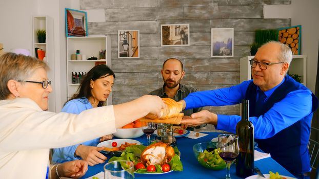 Man in his sixties serving his wife with bread at family dinner.