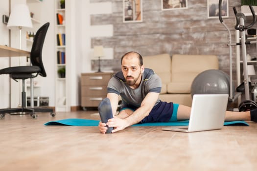 Man doing legs stretching on yoga mat from online training during global lockdown.