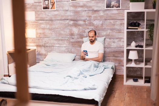 Man cheking social media before sleep in his cozy bed
