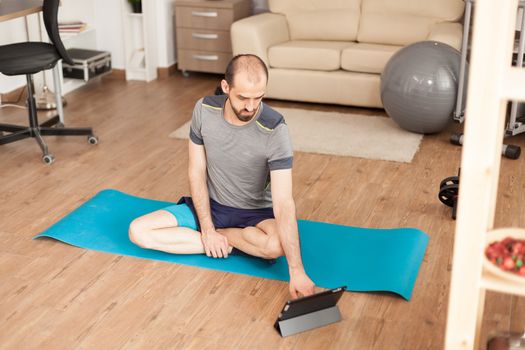 Calm man watching yoga class on tablet computer during global pandemic.