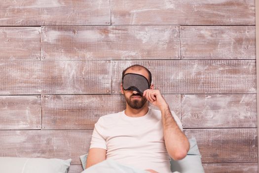 Caucasian man pulling his sleep mask wearing pajamas.