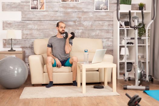 Man in sportswear holding dumbbells watching online training during global pandemic.